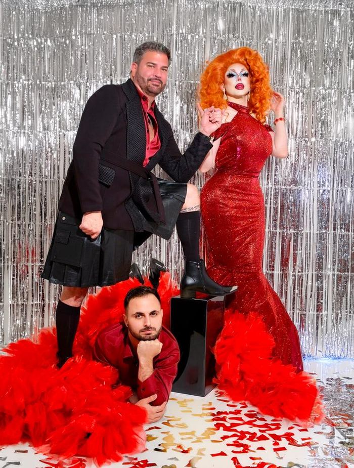 Camp Nackte co-owner JP and his partner Joel with their Unite the Fight drag coach, in glamorous red and black outfits against a silver tinsel backdrop
